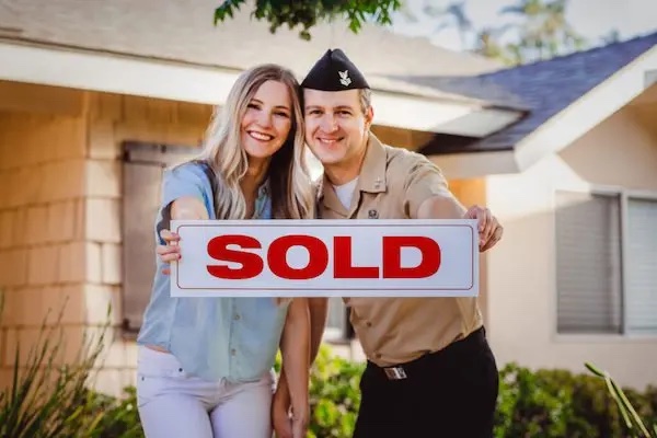 A couple holding a sold sign in front of a house