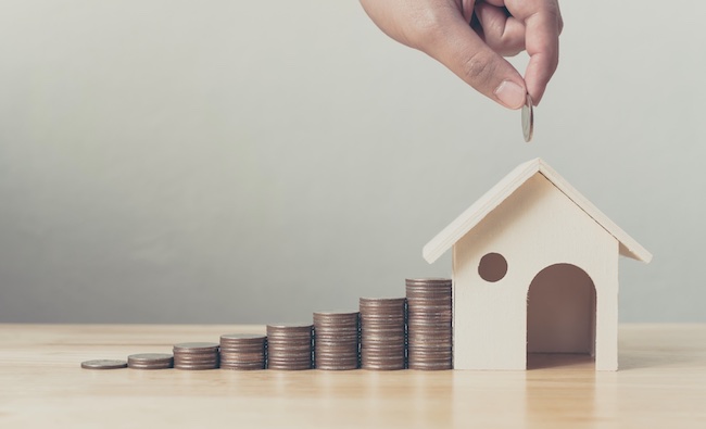 A hand stacking coins leading up to a model house