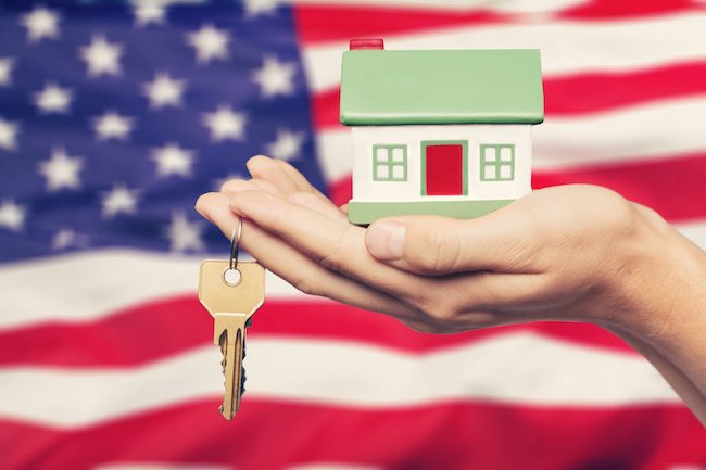 A hand holding a model house in front of an American flag