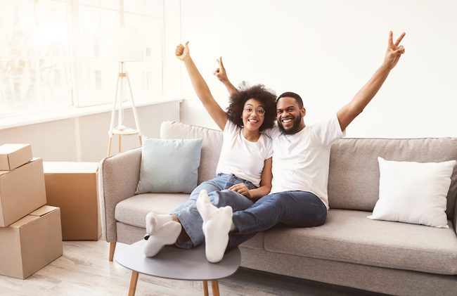 Couple on couch with hands in the air smiling